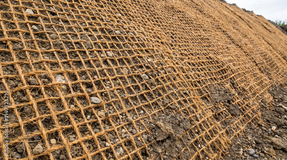 Fototapeta premium Sustainable coconut coir geotextile erosion control mat installed on a soil slope for environmental land stabilization