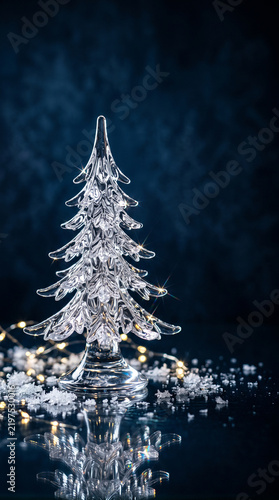 transparent crystal Christmas tree sculpture on a reflective surface, surrounded by delicate ice crystals and tiny sparkling light 