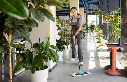 Фотография Cleaner woman janitor mopping office floor in uniform