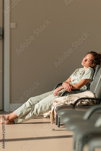 Healthcare worker in sage scrubs sleeping on waiting room chairs, an exhausted and depleted pose for medical wellbeing and burnout copy space