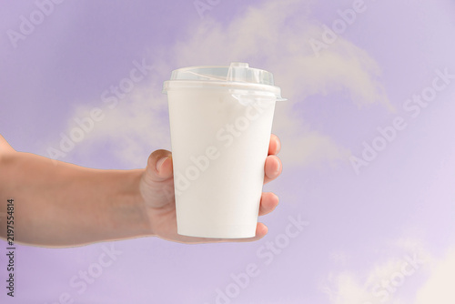 Foto A hand holds a white disposable cup against a soft purple background