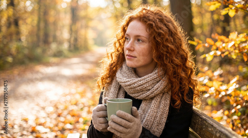 Redheaded woman holding a warm ceramic mug amidst golden autumn foliage in a serene forest.