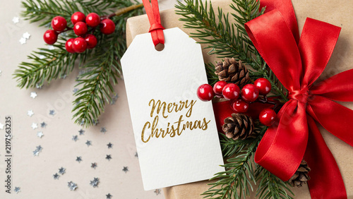 Close-up of Christmas gift tag with pine branches red berries and ribbon in natural light