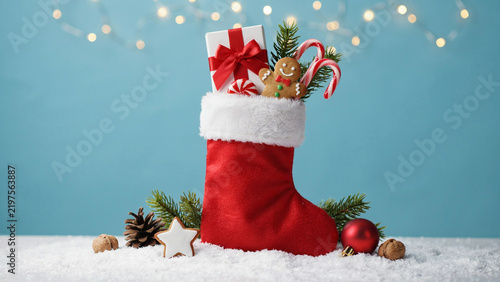 Christmas stocking filled with gifts and candy canes on snow with festive background