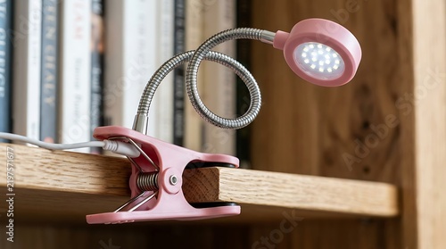 Pink LED clip lamp attached to a wooden bookshelf with a flexible neck