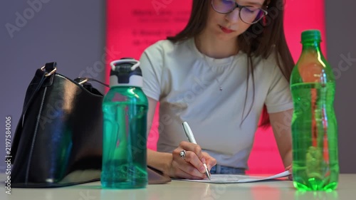 Focused young woman with glasses writing on document at desk