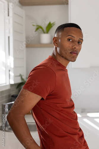 African American man wearing rust-red T-shirt leaning on white kitchen counter near stainless sink
