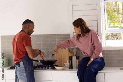 African American couple cooking at stove man denim apron stirring pan with spatula woman adding oil