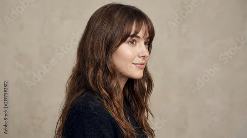 Young woman with long wavy hair poses in side profile. Soft studio light highlights her beauty against a neutral background with copy space. Portrait concept for beauty branding.