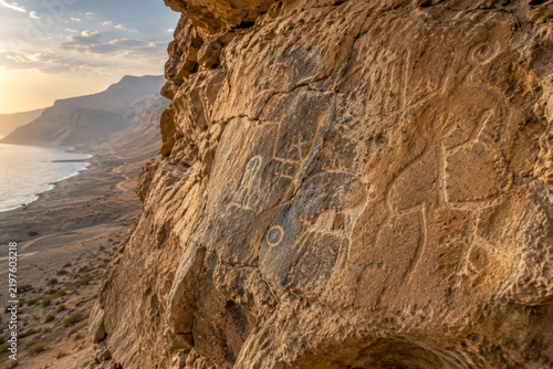 Ancient rock carvings weathered into desert cliff above coastal route