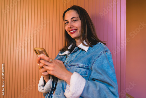 Portrait of smiling Caucasian female freelancer looking at camera holding smartphone indoors, presenting flexible remote work freelancing flexibility and modern digital nomad workflow