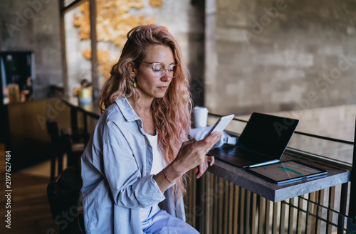 Obraz na plátně Focused Caucasian female user texting on smartphone while reviewing two factor s