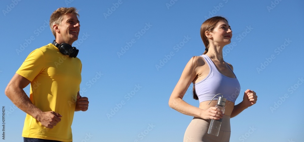 Obraz premium Sporty couple running under blue sky, low angle view