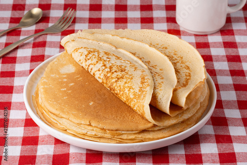 A stack of pancakes on a white plate on a red checkered tablecloth