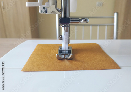 Obraz na płótnie Sewing machine: a metal presser foot is lowered onto a rectangular piece of mustard-brown fabric