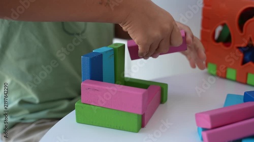 Slow motion footage of a child playing with colorful wooden building blocks on a table during an educational activity at home.