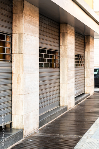 Bild auf Leinwand Vertical view of closed metal roller shutters and travertine pillars along a sho