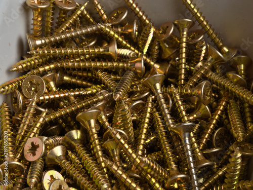 Konstfotografi Gold Zinc Wood Screws Pile Close-Up - Large pile of gold zinc-plated countersunk Phillips head wood screws filling a storage bin, macro detail view