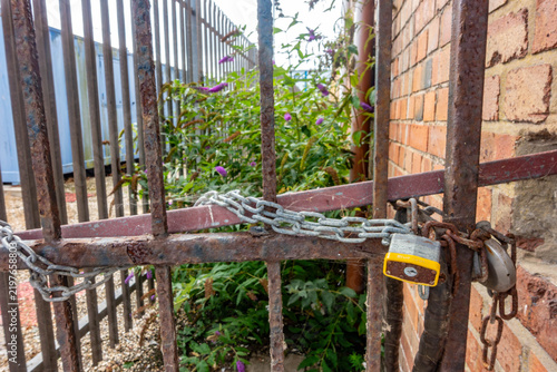 A rusty metal gate is secured with a locked padlock and metal chain