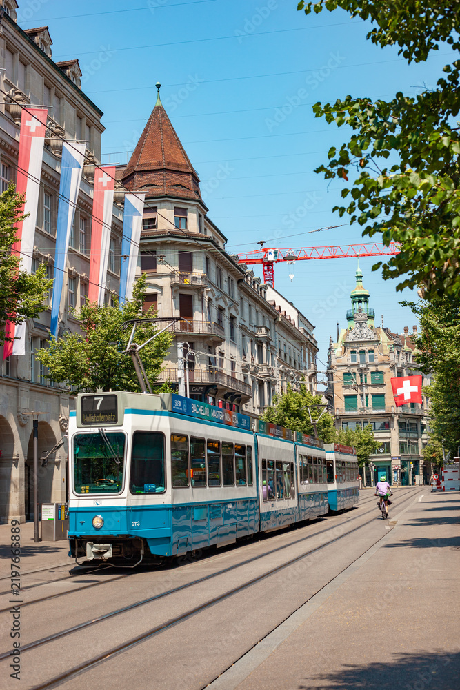 Fototapeta premium ZURICH, SWITZERLAND - JUNE 28, 2026: Blue public tram line 7 driving past historic buildings on Bahnhofstrasse in Zurich city center