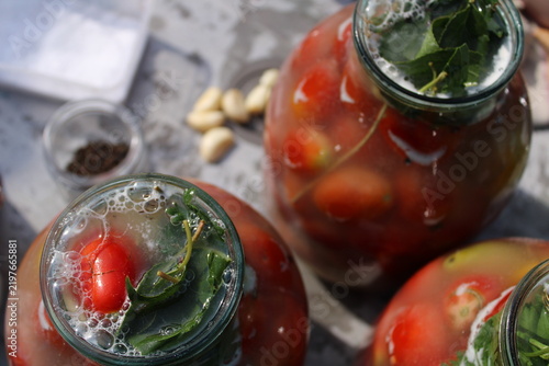 фотографія Glass jars filled with red tomatoes and herbs in brine for pickling, showcasing traditional home canning process with natural lighting