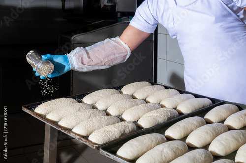 Bakery worker sprinkling sesame seeds on bread dough