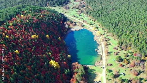 Lake surrounded by dense forest and vivid autumn foliage, with a rural road and meadow visible around the turquoise pond. Mengen, Bolu, Turkey 
