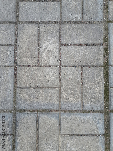 Gray Paving Stone Surface Background. Abstract background of paving tiles. Surface of geometrically laid bricks. Texture of gray paving slabs. Road surface aged by time and covered with moss and sand.