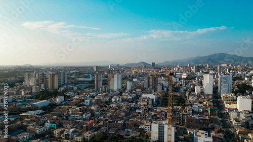 Panoramic aerial view of San Miguel city landscape featuring a tall yellow construction crane over residential buildings with distant Andes mountains