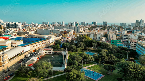 Aerial drone view of a vibrant public park featuring colorful outdoor sports courts and recreation areas near the coastline in San Miguel Lima