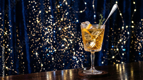 Elegant cocktail glass with ice and garnish against a festive blue bokeh light background.