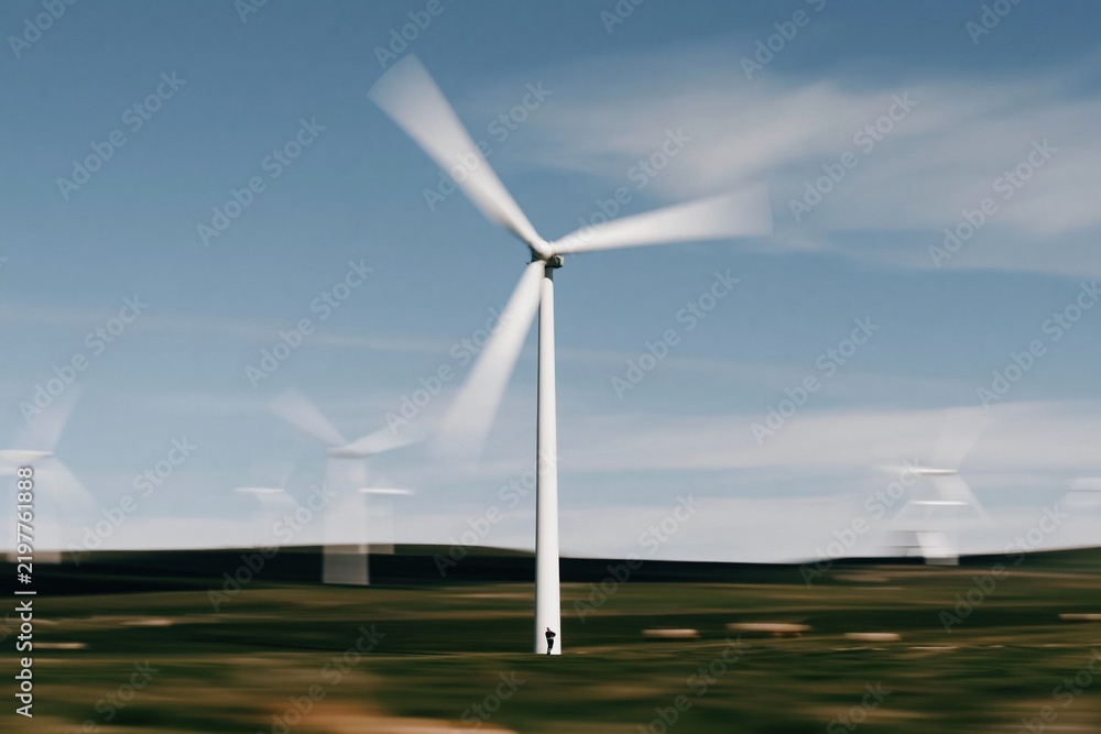 Obraz premium Motion blurred wind turbine spinning generating clean renewable energy on a sunny day with a clear blue sky