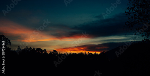 Dramatic colorful sunset over silhouetted forest and mountains