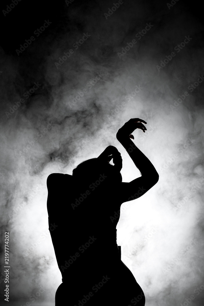 Obraz premium silhouette modern ballet dancer posing on dark background with smoke