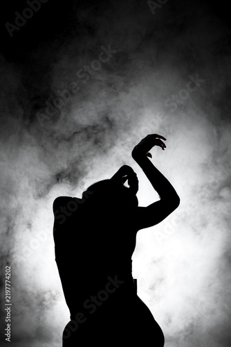 silhouette modern ballet dancer posing on dark background with smoke