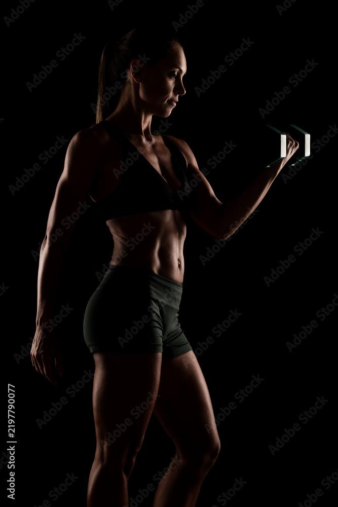 Fototapeta premium Woman Lifting Dumbbells Demonstrating Strength and Fitness in a Dark Studio Setting