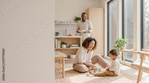 Happy family spending quality time together, mother and child playing with building blocks in living room while father prepares food in kitchen at home