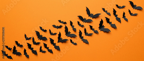 Black paper bats swarm on orange background for Halloween.