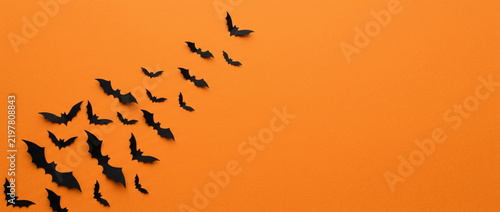 Black paper bats flying across orange background, Halloween theme, copy space