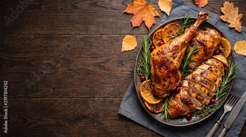 Roasted turkey dinner with autumn leaves on dark wood background, festive thanksgiving meal with sliced poultry and rosemary, traditional holiday food flat lay