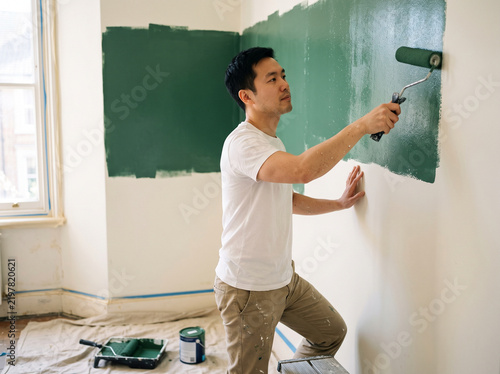 East Asian man in his 30s painting a wall during redecoration