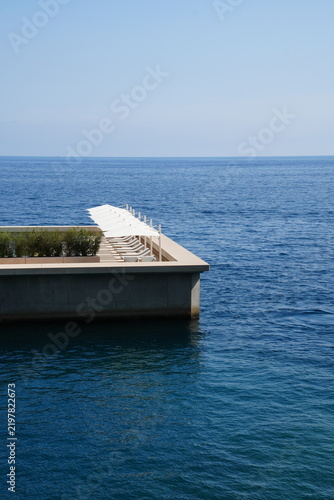 Canvastavla Modern seaside deck with a row of white sun loungers and umbrellas overlooking a vast blue sea under a pale, cloudless sky