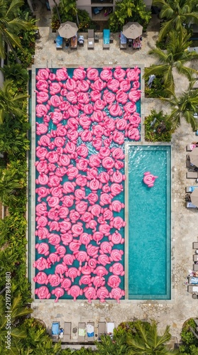 Aerial View of Swimming Pool Surrounded by Pink Floats and Lounge Chairs in a Tropical Resort.