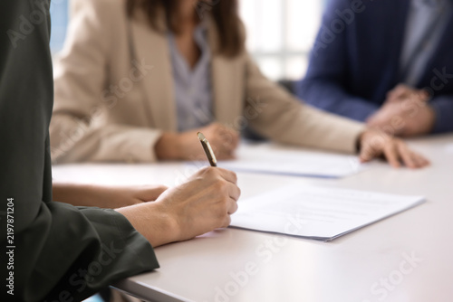 Close up businesswoman signing agreement on paper document at meeting table closing business deal with partners completing signature on employment contract affirming insurance or investment paperwork