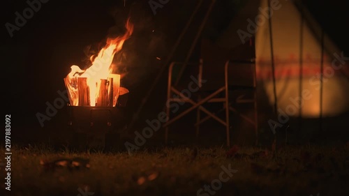 夜のキャンプ場で燃え盛る焚き火の炎と温かく照らされるワンポールテント
