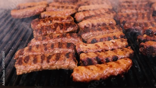 Traditional Romanian mici (grilled minced meat rolls) and susages cooking on a barbecue grill at a local fair, with smoke rising from the hot coals and the atmosphere of a Romanian outdoor food festiv