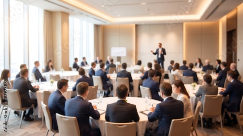 Professional speaker presenting to group of business people at round tables during corporate workshop in bright hotel conference venue with soft natural lighting and blurred background