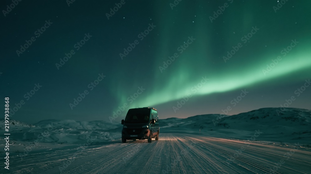 Naklejka premium Van driving on snowy road under northern lights