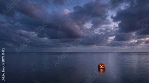 Glowing Halloween pumpkin floating alone on a dark sea