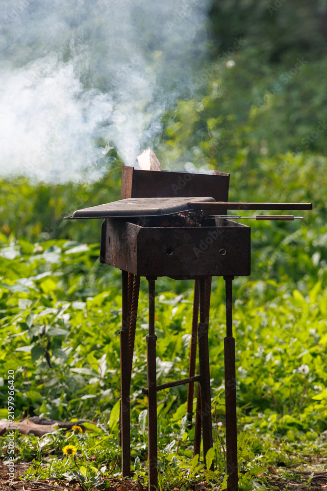 Fototapeta premium Smoke rises from a rusty outdoor grill